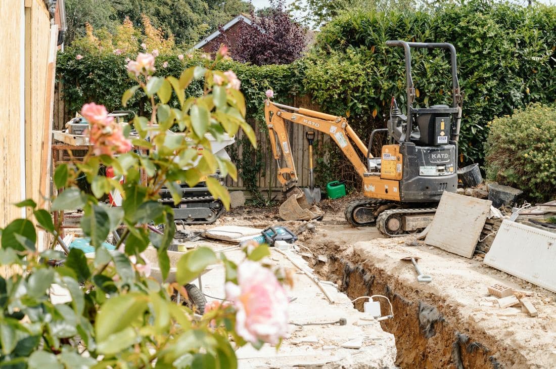 A mini digger working on a trench in a backyard garden